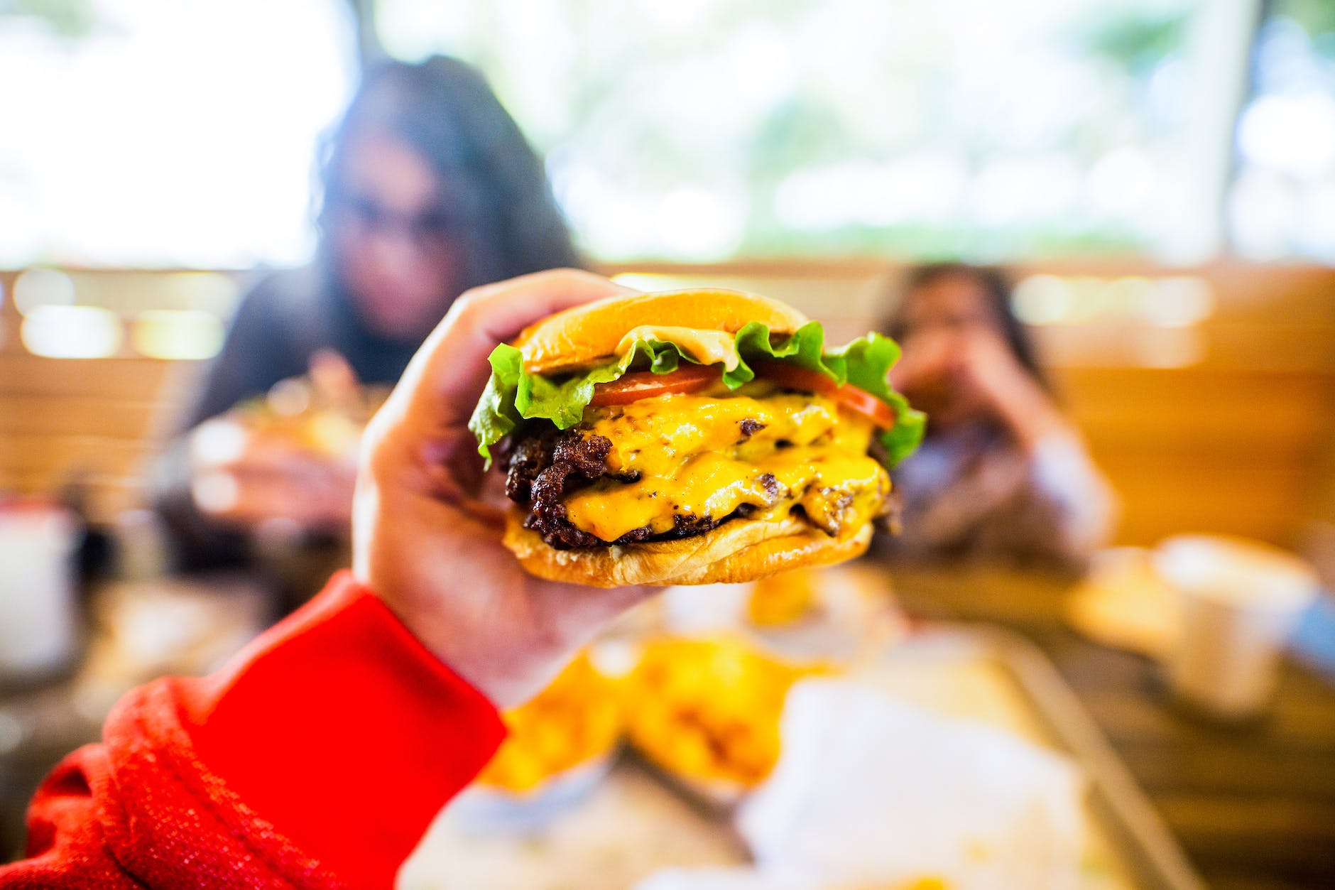 person showing delicious cheeseburger in cafe